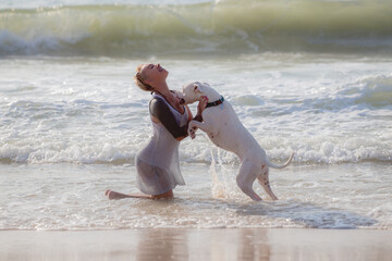 Woman enjoy playing on beach with white Dogo Argentino