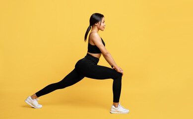 Fototapeta na wymiar African american lady in sportswear stretching legs before workout, preparing for sport training on yellow background