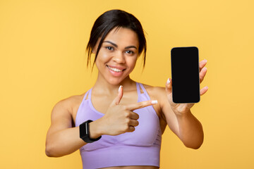 New fitness appication. Sporty african american woman pointing at smartphone empty screen for mockup template