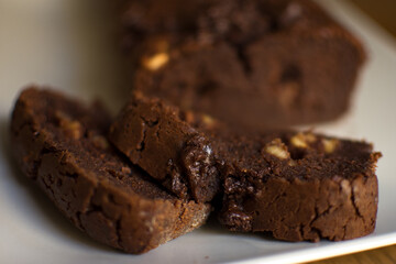 two pieces of chocolate and walnut brownie cake on a white plate and the rest of the cake is out of focus in the background - front view