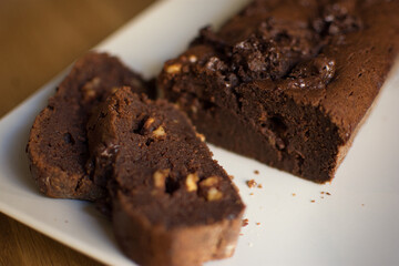 chocolate and walnut brownie cake cut, in front of him two pieces on white plate on brown wooden table - front top view to the left