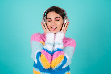 Young woman in a bright multicolored sweater on a blue background in large noise canceling...