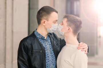 Young gay couple wearing medical mask hugging at city.