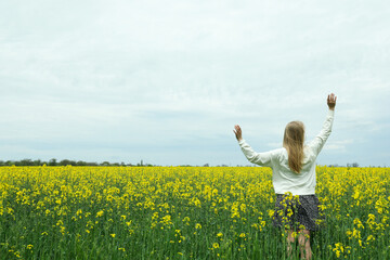Fototapeta premium A girl stands in a rapeseed field on a summer day