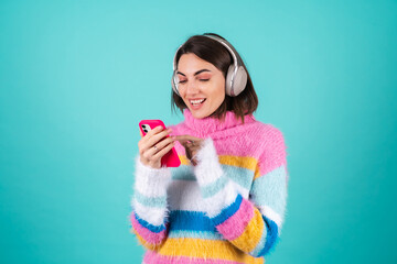 Young woman in a bright multicolored sweater on a blue background in large noise canceling...