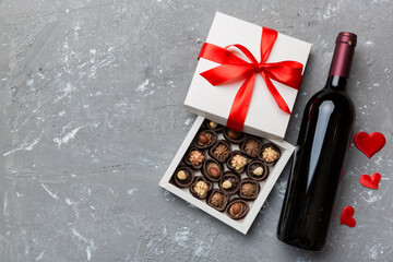 Bottle of red wine on colored background for Valentine Day with gift and chocolate. Heart shaped with gift box of chocolates top view with copy space