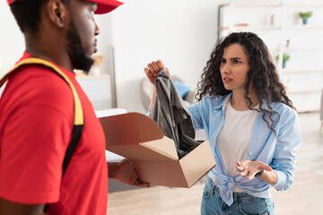 Confused angry lady unpacking box, holding clothes