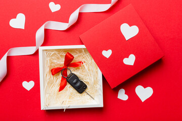 Black car key in a present box with a ribbon and red heart on colored background. Valentine day composition Top view
