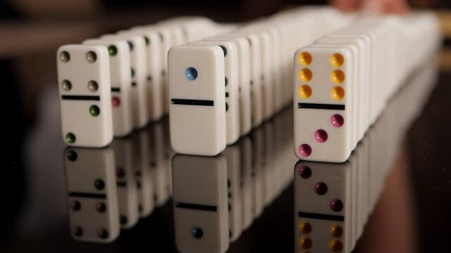 Three rows of dominoes are slowly falling on a black mirror background. Concept of domino effect and chain reaction.