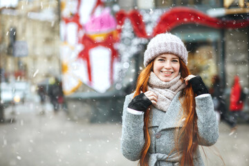 Joyful ginger lady walking at the city with snowflakes