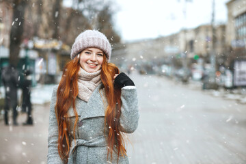 Expressive ginger lady walking at the city with snowflakes