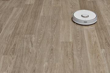 The robot vacuum cleaner is working on cleaning the room. Cleaning the laminate. Cleaning concept.