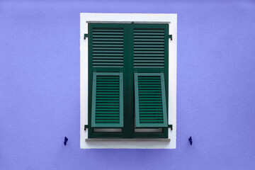 green wooden window with shutters in white frame on blue violet wall