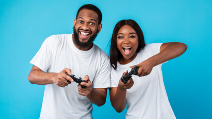 Excited African American couple playing video games together with joysticks © Prostock-studio