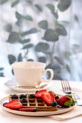 Waffles made from spelled flour and whole grain flour for breakfast. Strawberries and blueberries in a plate. The concept of proper nutrition.
