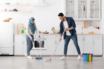 Loving muslim couple cleaning floor in kitchen
