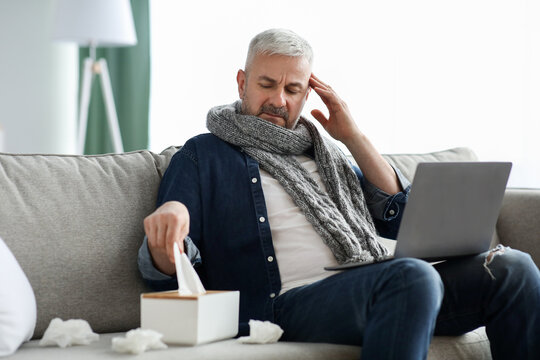 Sick mature man with laptop websurfing, home interior