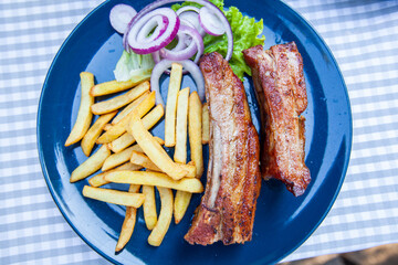 Grilled pork ribs with French fries and onion. Serving on plate at restaurant table.
