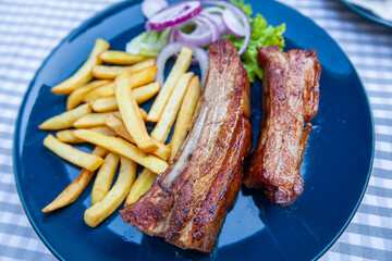 Grilled pork ribs with French fries and onion. Serving on plate at restaurant table.