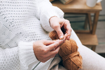 A middle-aged woman is engaged in home handicraft knitting, knitting with threads. Home activity hobby during free time