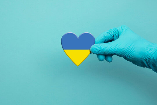 Medical workers hand wearing surgical glove holding Ukraine flag heart - Powered by Adobe
