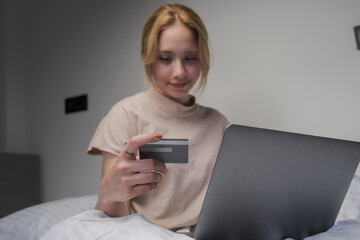 woman browsing social media on laptop in bed, blonde woman shopping online with laptop in bed in the morning