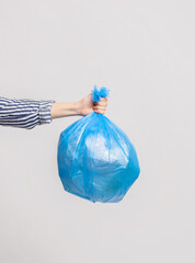 Female Hand Holding Blue Plastic Bag With Garbage Over Light Grey Background