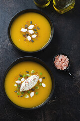 Pair of black bowls with pumpkin cream-soup, vertical shot on a dark brown stone background, top view