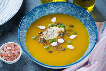 Blue bowl with pumpkin soup topped with soft cheese and pumpkin seeds, middle close-up, studio shot