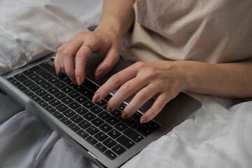 Fototapeta na wymiar woman browsing social media on laptop in bed, woman shopping with credit card and laptop on bed with white cover, shopping online in bed