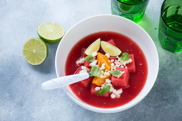 White bowl with gazpacho cold soup made of watermelon, elevated view on a light-blue stone background, horizontal shot