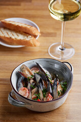 mussels with sauce and grilled bread in plate on wooden table with glass of white wine near and dark background. restaurant concept