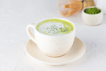Matcha tea with coconut milk and a whisk in a light mug.
