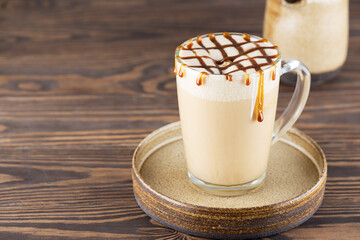 Caramel macchiato with coconut cream in a glass mug on a wooden table. Horizontal orientation, copy space.