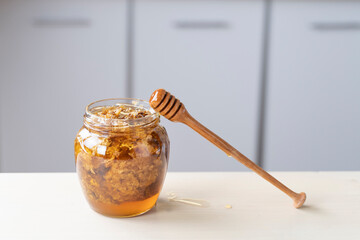 Golden honeycomb and beeswax in a jar of honey on the table. Sweet organic honey in a jar with a wooden stick closeup. Background for beekeepers, healthy nutrition organic food