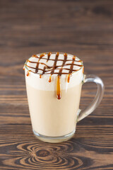 Vegan caramel macchiato with coconut cream in a glass mug on a wooden table.