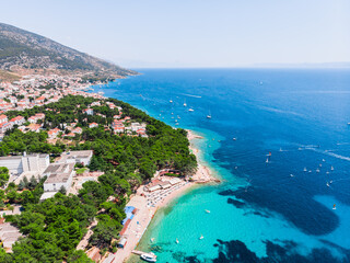 Drone shot at a windsurfing school on the island of Brac in Croatia. People are relaxing on the beach. View from a drone on sunbathing tourists on sun loungers. The resort town of Bol view from drone - obrazy, fototapety, plakaty