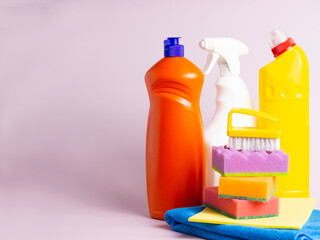 cleaning products for home on a purple background copy space. Cleaning and general cleaning concept. Detergent bottles, brush, sponge and rags