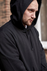 Dangerous caucasian bearded man in the hood, in black wear, confident serious hooligan standing outdoors looking at side, waiting for rape, victim. Stranger person, Bandit male at street.