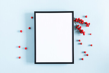 Christmas holiday composition. Photo frame, Xmas white decorations and red berries on pastel blue background. Christmas, New Year, winter concept. Flat lay, top view, copy space