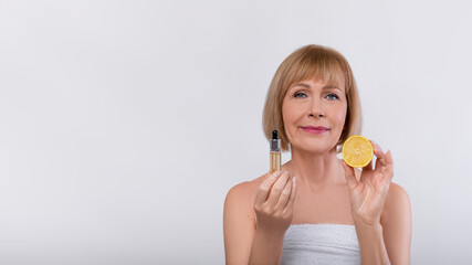 Sensual mature woman advertising organic cosmetics, showing moisturizing serum with fruit acids and lemon