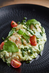 risotto with pesto, basil and cherry tomatoes closeup in black plate on wooden table. risotto on wooden table restaurant