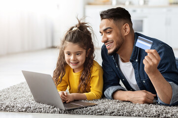 Happy arab dad and daughter with laptop and credit card shopping online