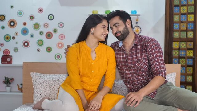 An attractive couple in casual clothes hugging each other while sitting in bed. Cheerful husband-wife posing for the camera at home - leisure time  relaxation  nuclear family  Indian couple