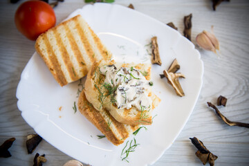 fried bread toast with cheese spread with boiled dried mushrooms on a wooden table.