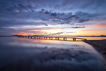 Obraz premium Photograph of a sunrise in the Mar Menor, in the region of Murcia, Spain. There is a jetty over the calm waters of the sea and colorful clouds reflecting in the water
