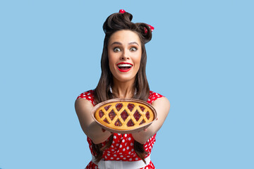 Positive pin up woman in retro style dress holding yummy homemade pie on blue studio background
