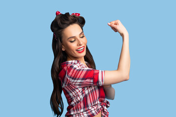 Sensual pin up woman in retro clothes showing her strong biceps muscles on blue studio background
