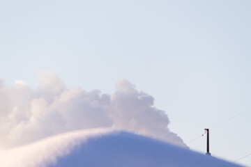 Roof top covered with snow and smoke in blue sky on winter day on background
