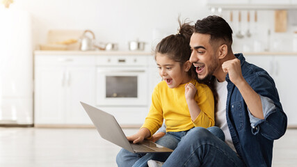 Internet Win. Portrait Of Excited Arab Dad And Daughter Looking At Laptop